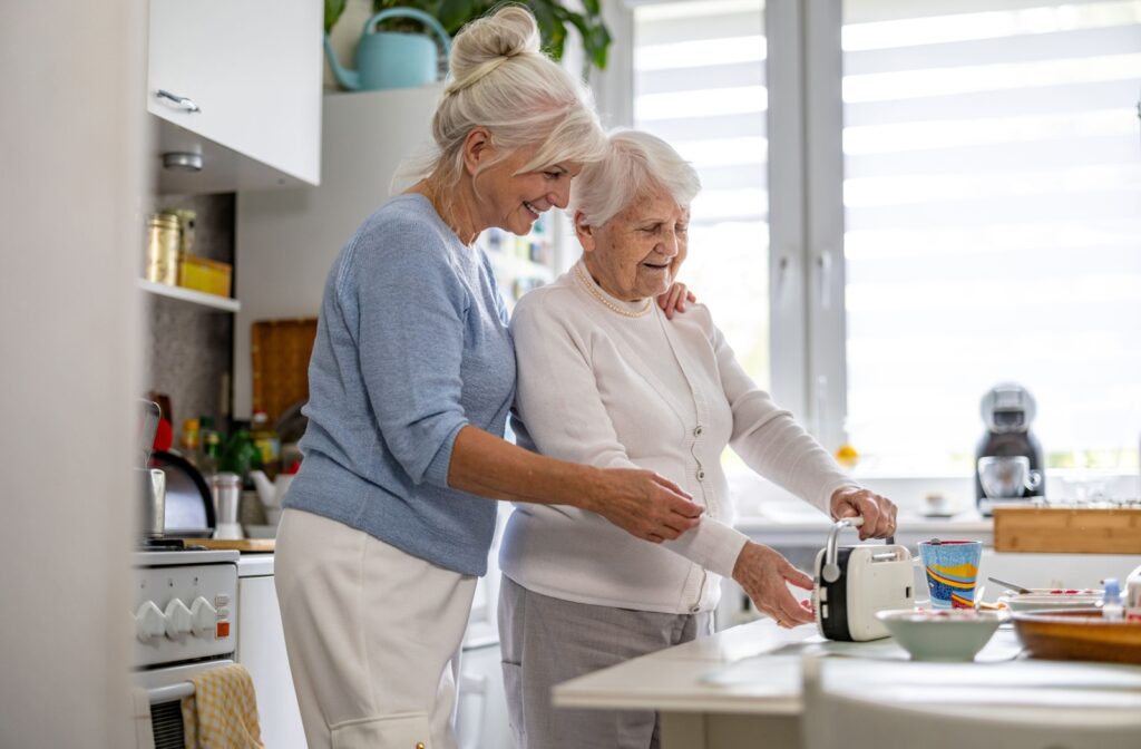 Older parent with their adult child in a kitchen, smiling and working together to operate a kitchen appliance.