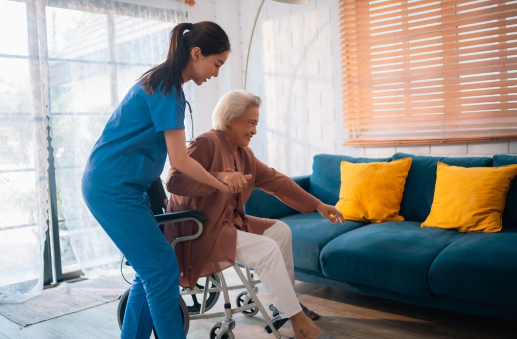 A senior care worker helps someone from their chair to their couch.