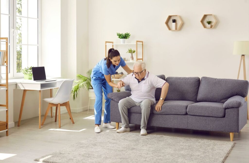 a carer helps a senior stand from a couch