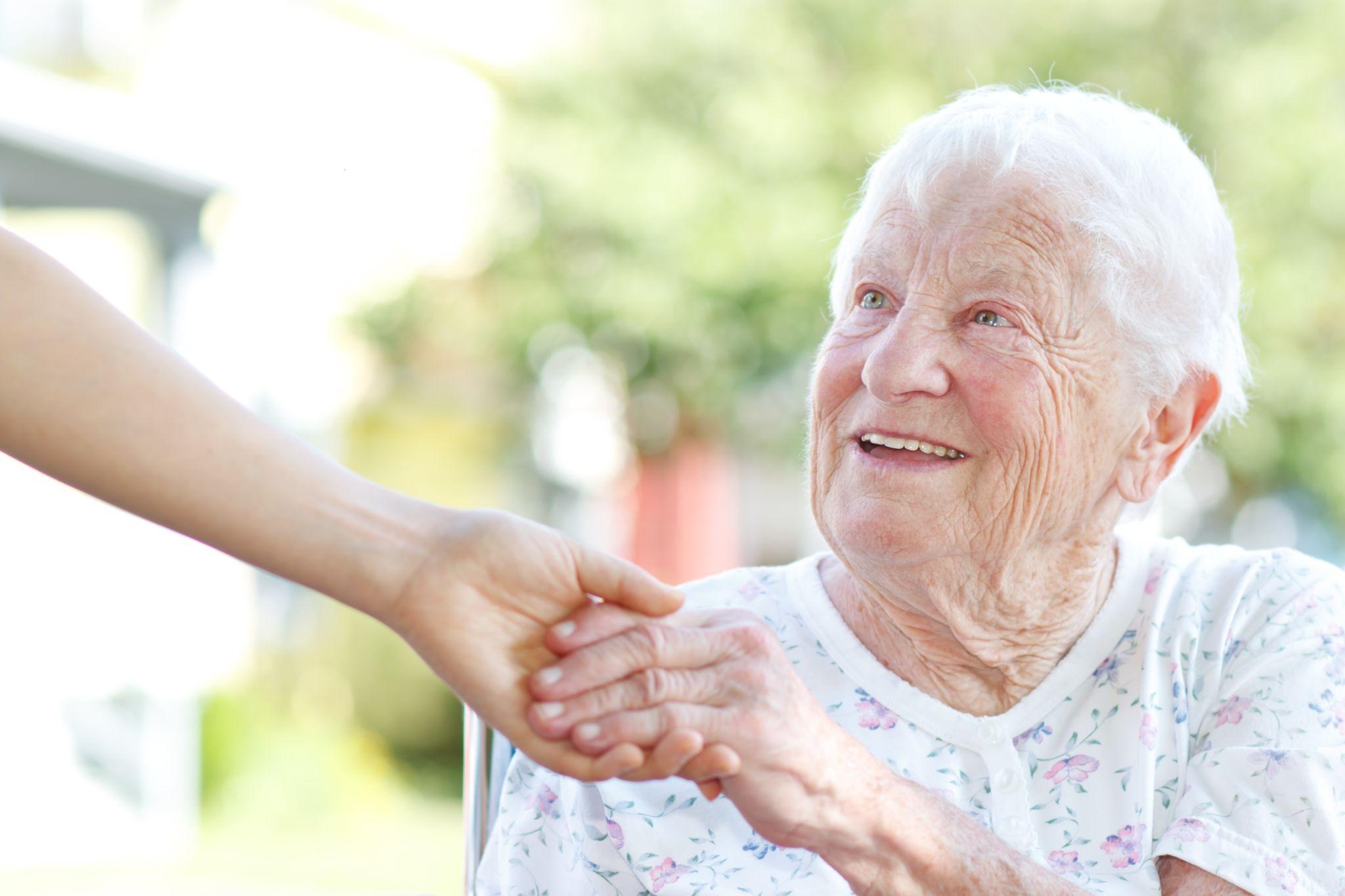 a smiling senior holds the hand of a caregiver